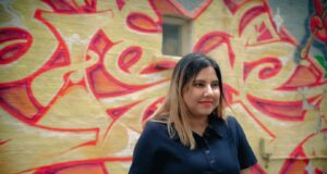 A person standing in front of a wall with graffiti Description automatically generated