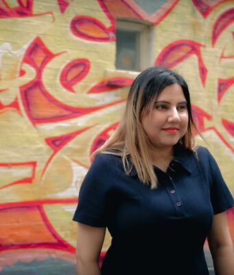 A person standing in front of a wall with graffiti Description automatically generated